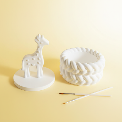 White plaster giraffe trinket box lid off with paintbrushes on lemon yellow and cream background