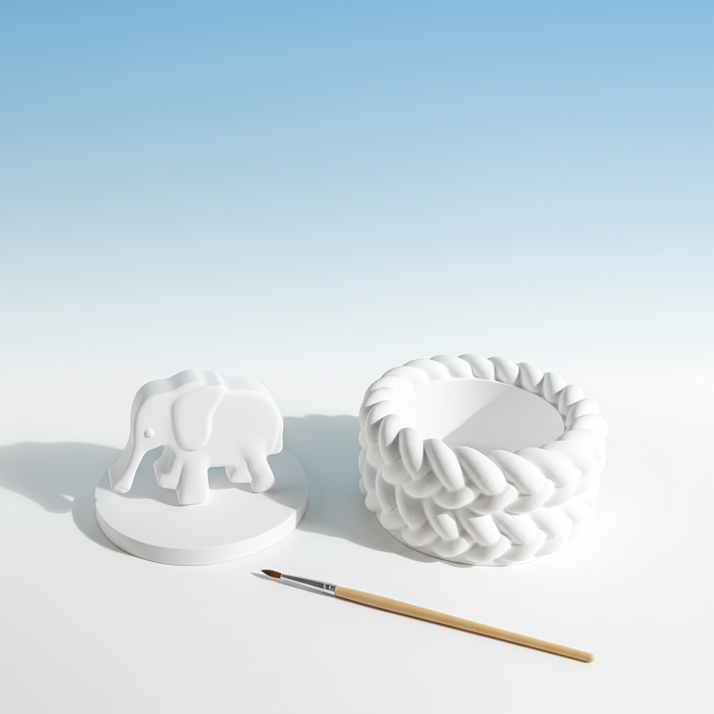 White plaster elephant trinket box lid off with paintbrush on sky blue and white background