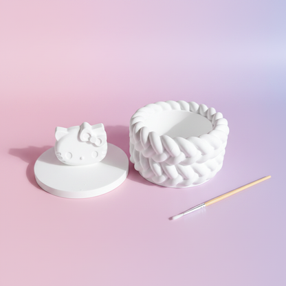 White plaster cartoon cat face trinket box lid off with paintbrush on pink and lilac background