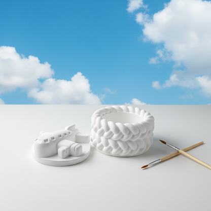 White plaster aeroplane trinket box lid off with paintbrushes on bright blue sky and fluffy clouds background