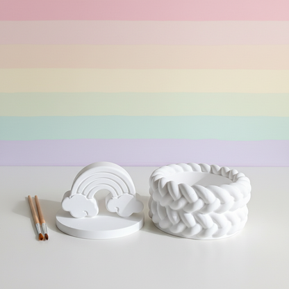 White plaster rainbow trinket box lid off with paintbrushes on soft pastel rainbow stripe background